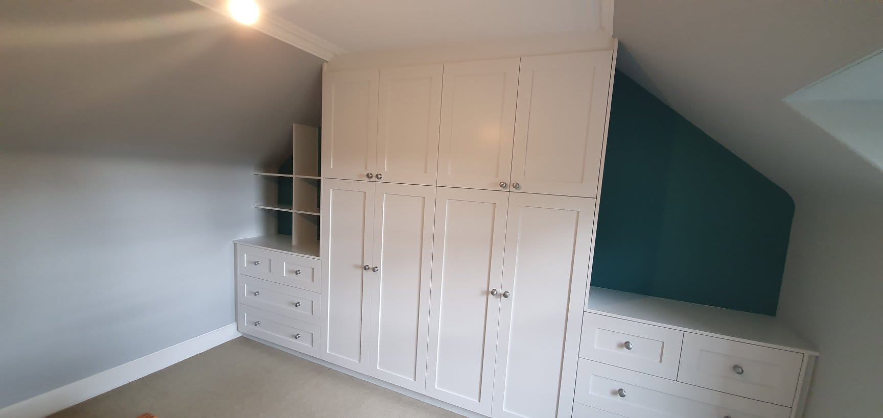 White fitted wardrobes beside a contrasting blue-green wall
